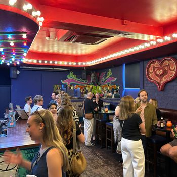 A bustling, brightly decorated bar (red ceiling, blue walls), filled with people smiling and chatting.