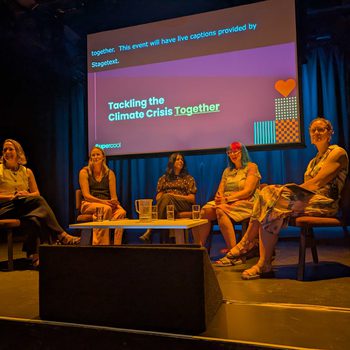 Five woman sat in a semi-cricle around a coffee table on stage at a conference, with a screen behind that reads "Tackling the climate crisis – together"