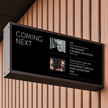 On an acousitc wooden-slat panelled wall, a black rectangular venue screen sticks out at 90 degrees. The screen reads "Coming next", and displays 2x event images, titles, dates and times