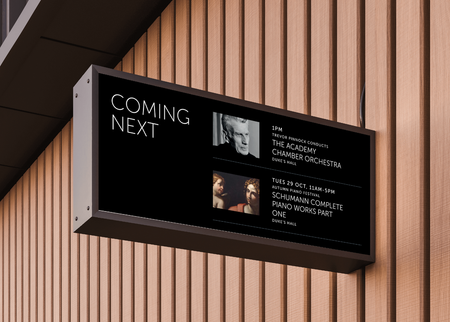 On an acousitc wooden-slat panelled wall, a black rectangular venue screen sticks out at 90 degrees. The screen reads "Coming next", and displays 2x event images, titles, dates and times