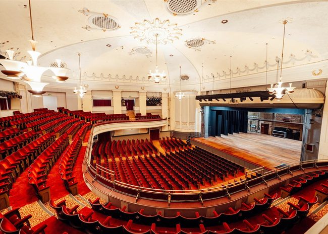 Bournemouth Pavilion's auditorium with rows of differnt levels of curved seating. The red chairs all facing towards the stage over on the rigth of the image.